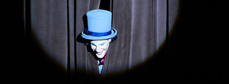 Image of drama performer sticking his head out of the curtain.